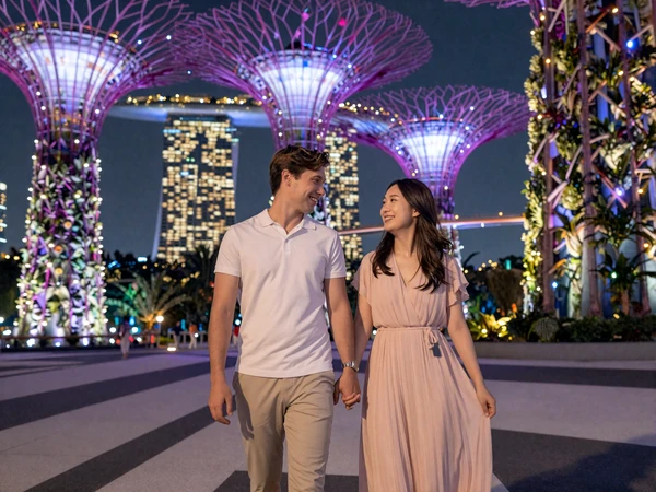 Happy cross-cultural couple walking through the illuminated Supertree Grove at Gardens by the Bay in Singapore at night