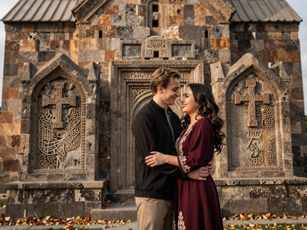 Happy cross-cultural couple embracing in front of an ancient Armenian stone church with khachkar cross-stones in autumn light