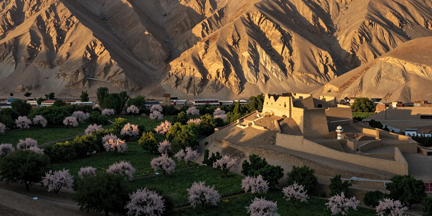 Dramatic Hindu Kush mountain landscape in Afghanistan with ancient fortress and lush valley at golden hour representing Afghan cultural heritage